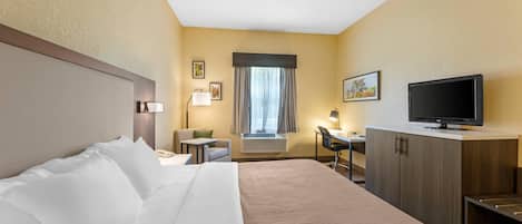 A hotel room with a bed, desk, TV, and window with curtains.