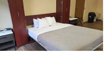 A hotel room with a bed, a desk with a telephone, and a trash bin.