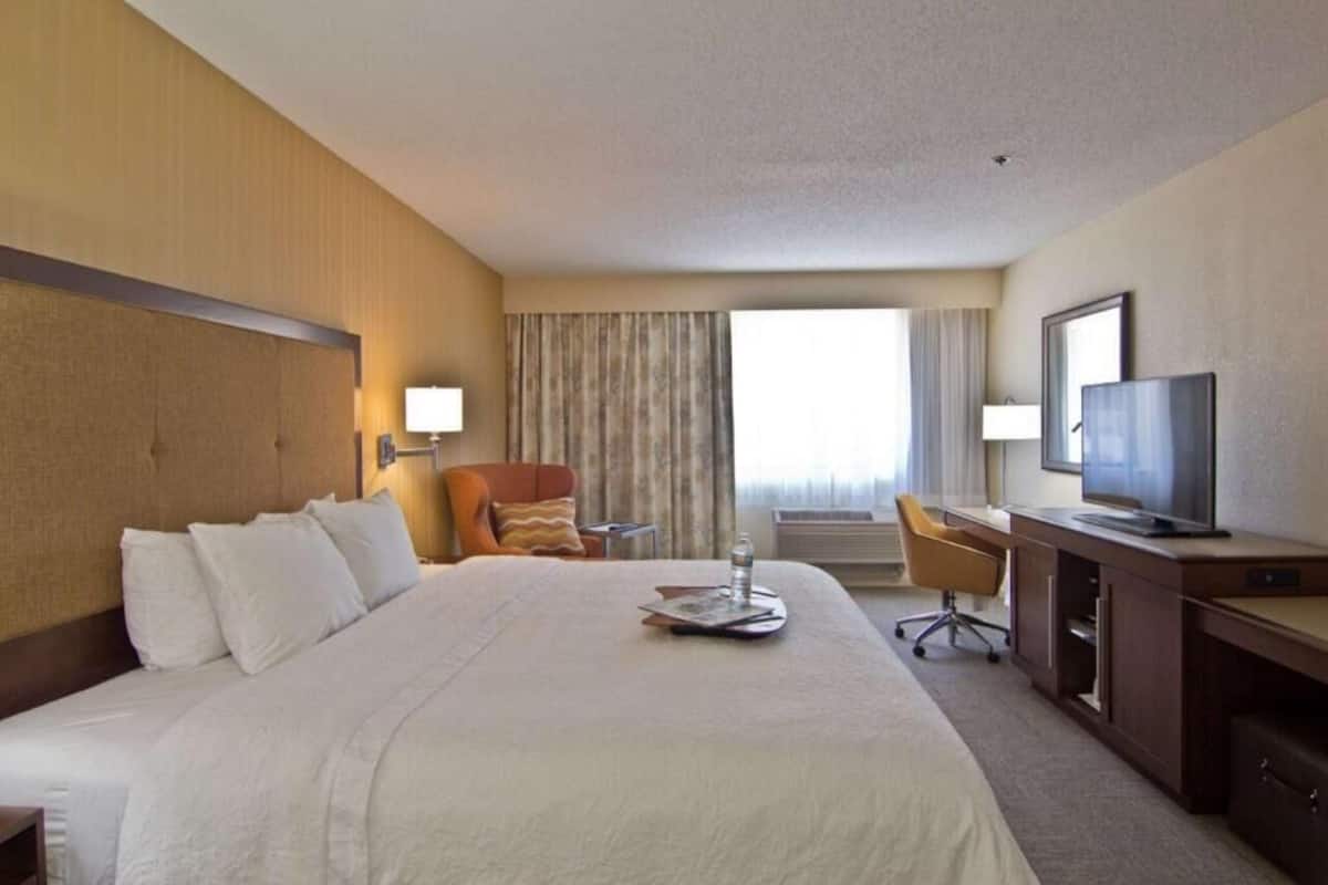 A hotel room with a large bed, a desk, a chair, a television, and a window with curtains.