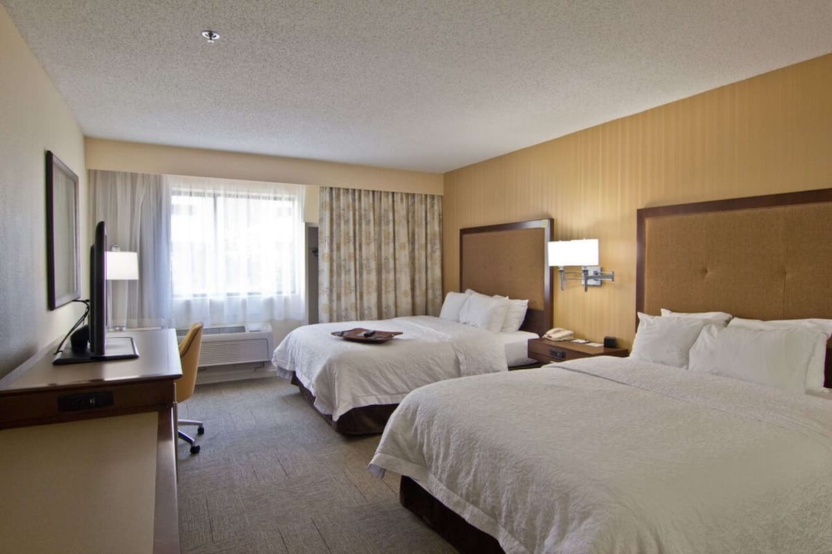 A hotel room with two beds, a desk, a chair, a TV, and a window with curtains.