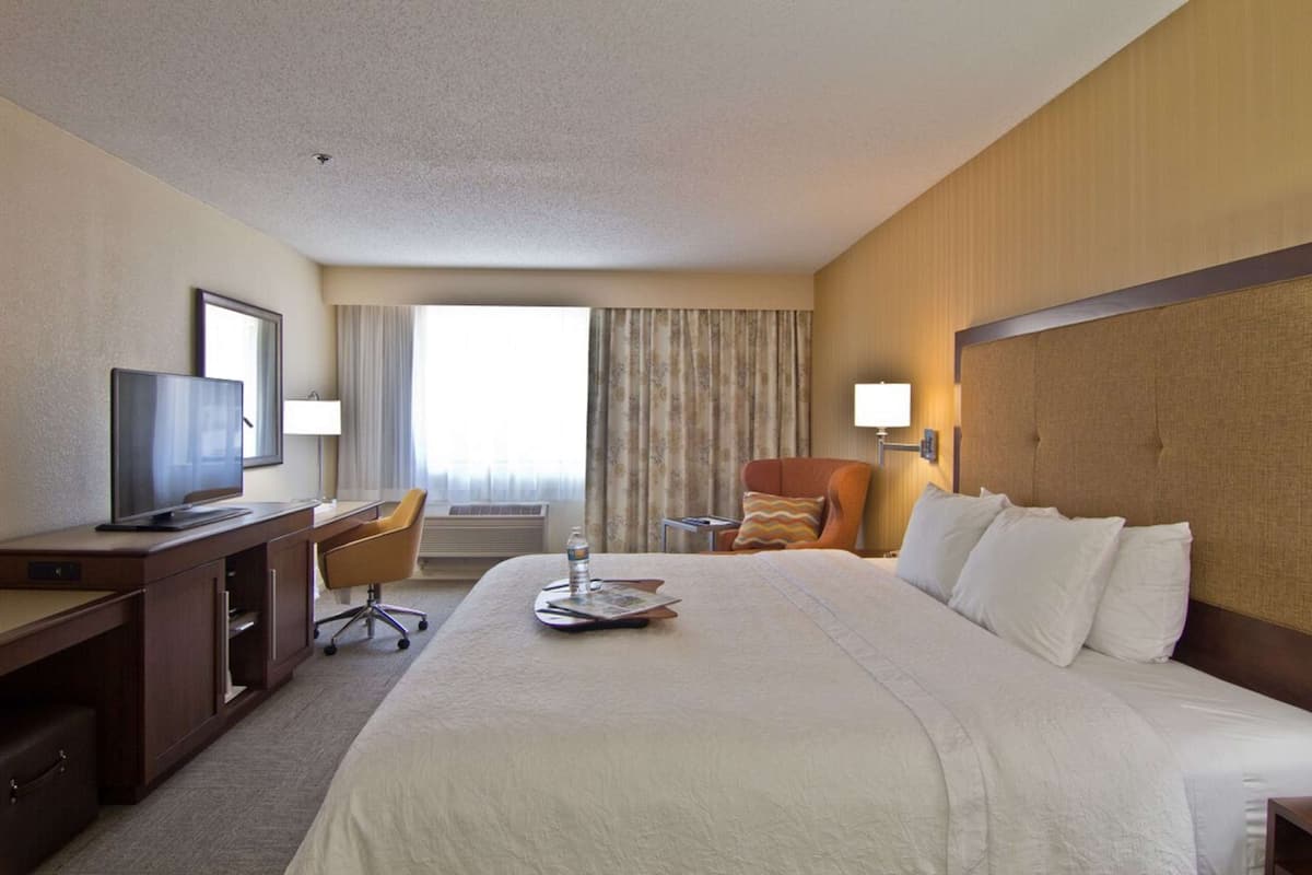 A hotel room with a large bed, a desk with a computer, a TV, and a window with curtains.