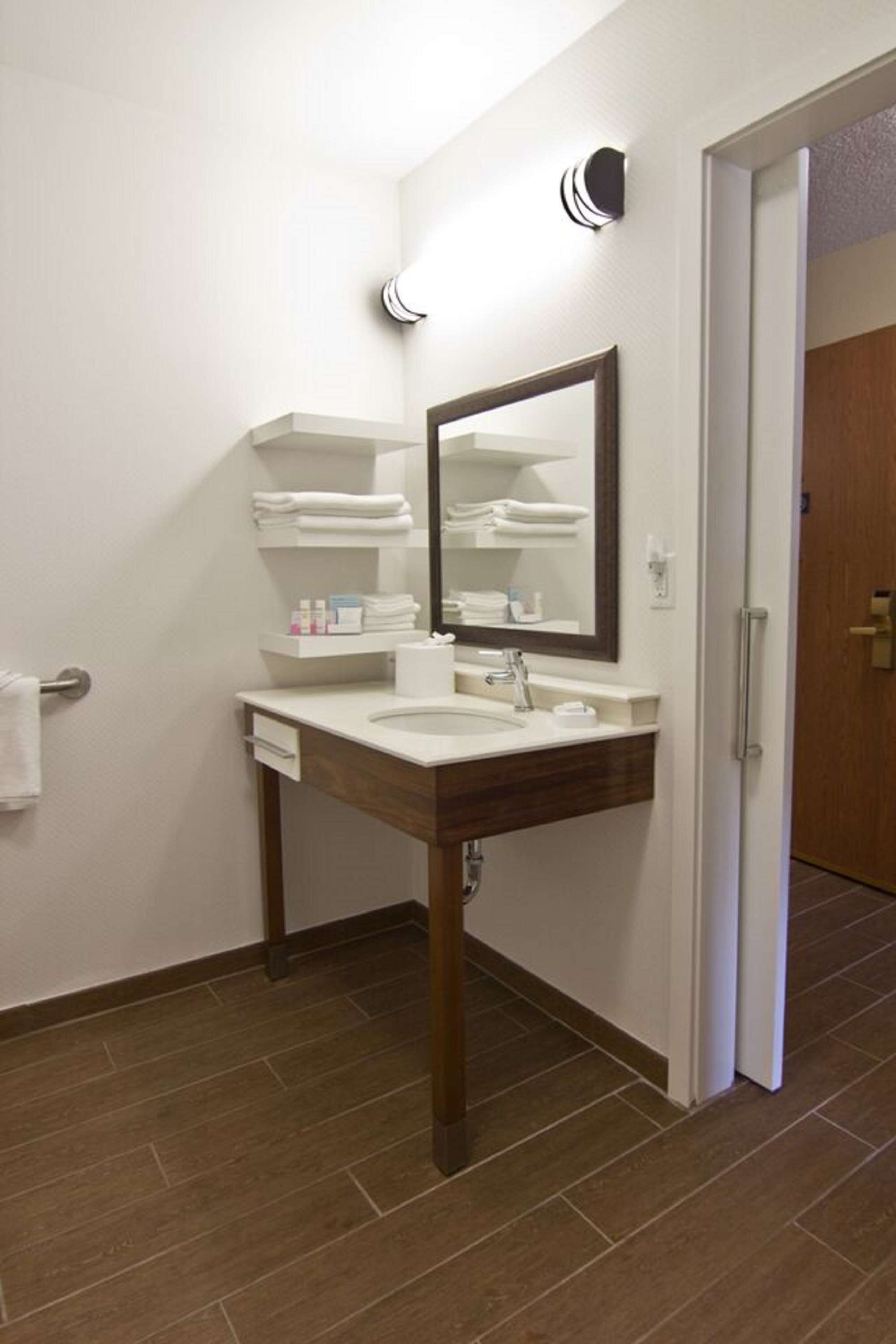 A bathroom with a white sink, a wooden vanity, a mirror, and a towel rack.