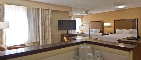 A hotel room with a bed, a desk with a computer, a TV, and a bathroom mirror.