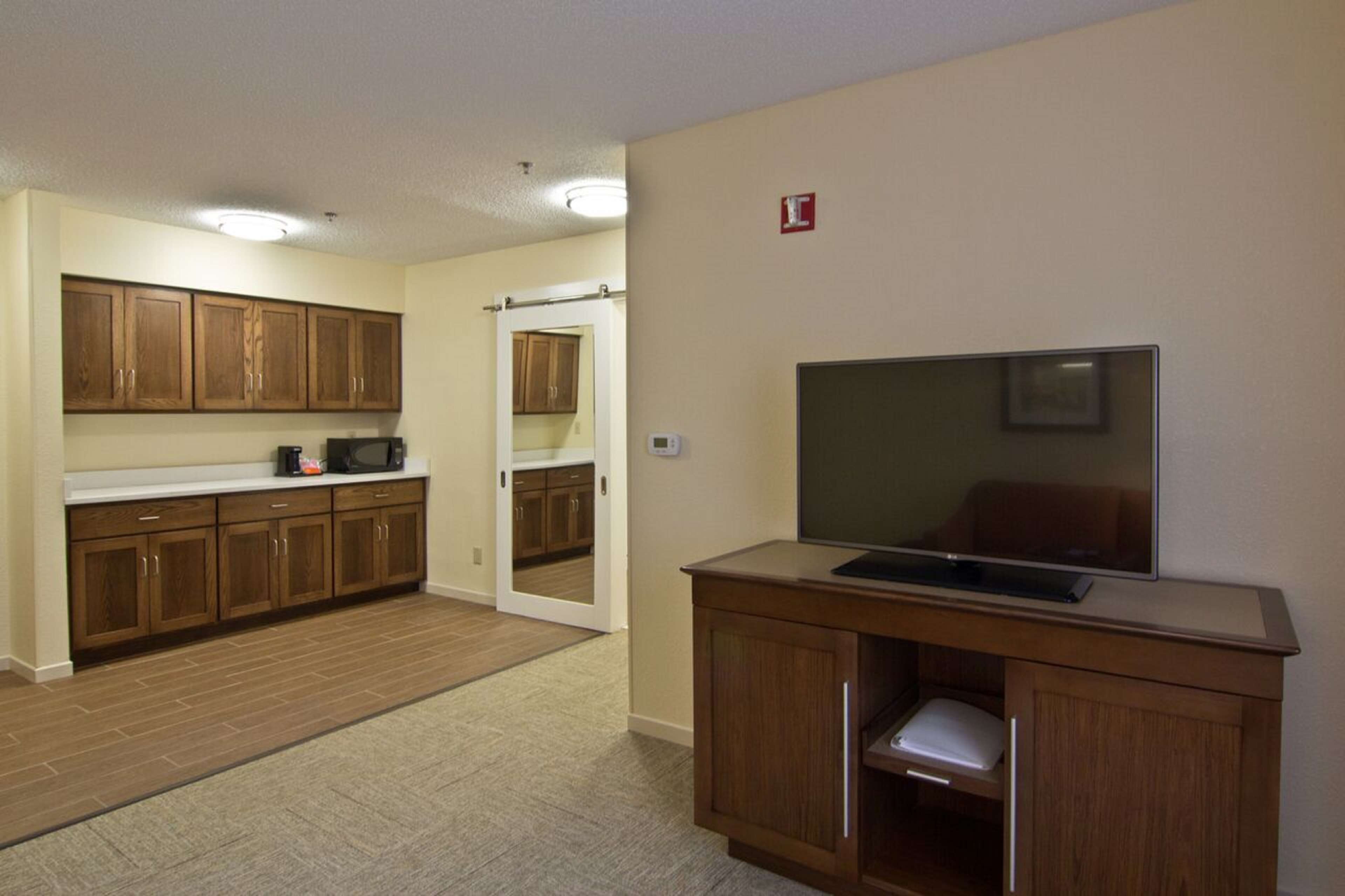 A compact kitchen with wooden cabinets, a microwave, and a television on a stand.