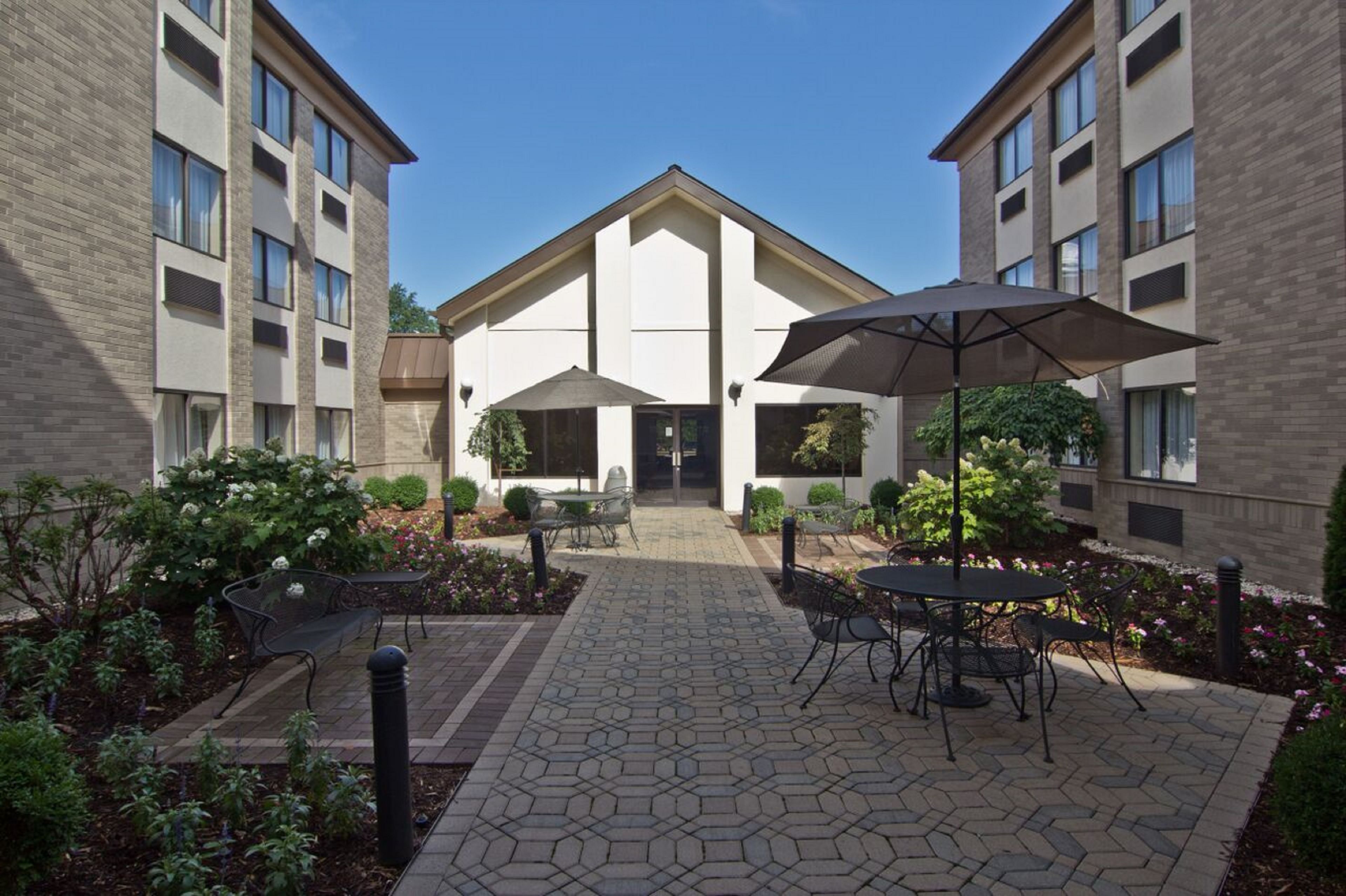 A courtyard with outdoor seating, a central building, and surrounding greenery.