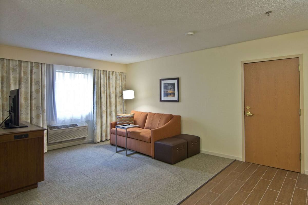 A hotel room with a sofa, a small table, a TV on a wooden cabinet, a picture on the wall, and a door.