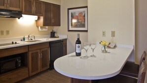 A kitchen with wooden cabinets, a white countertop, a built-in oven, a dishwasher, and a wine bottle with glasses on the counter. - Hampton Inn & Suites Chillicothe (Chillicothe)