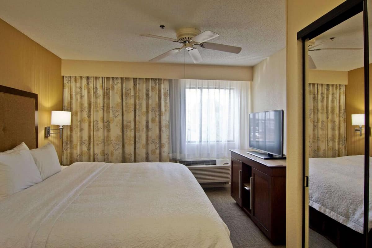 A hotel room with a large bed, a television on a wooden cabinet, a ceiling fan, and a window with curtains.