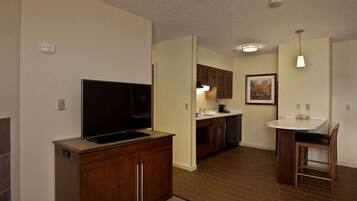 A modern kitchen with wooden cabinets, a built-in TV, a dining area with a table and chairs, and a pendant light.