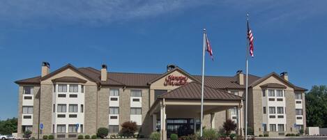 A Hampton Inn hotel with a two-story building, a covered entrance, and two American flags.