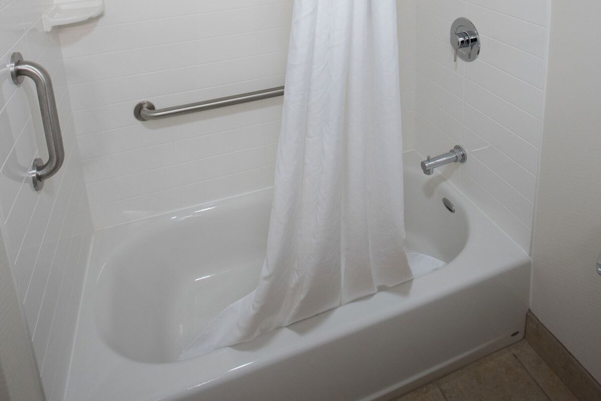 Una bañera blanca con cortina de ducha, barras de apoyo y ducha de mano.