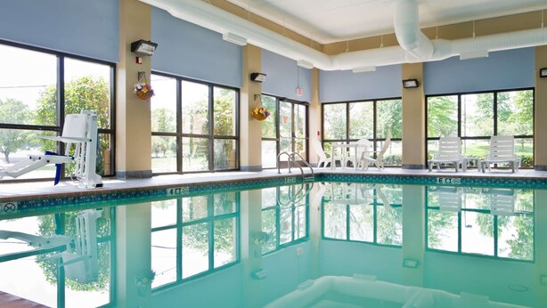 Una piscina interior con paredes de vidrio transparente, varias ventanas y algunas sillas de descanso.