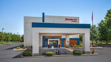 Un Hampton Inn by Hilton con entrada despejada, bandera estadounidense y jardines bien cuidados.
