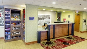 Zona de recepción de hotel con un mostrador de recepción, un cartel que dice 'Bienvenido a Wooster', un cartel de 'Suite Shop' y un cartel con la palabra 'Sonrisa'.