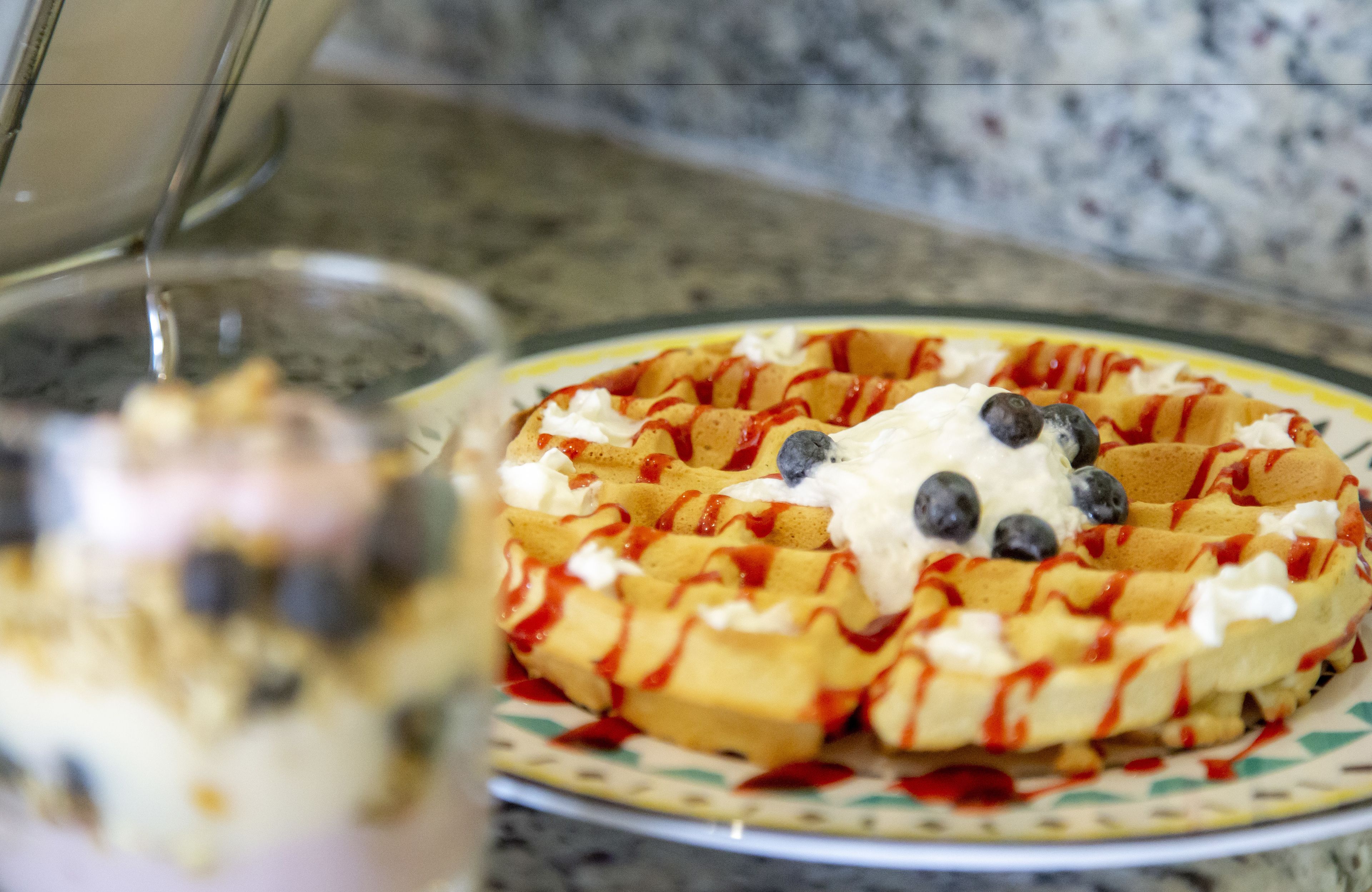 Un gaufre garni de crème fouettée et de myrtilles, le tout nappé de sirop.