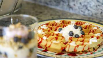 Un gaufre garni de crème fouettée et de myrtilles, le tout nappé de sirop.