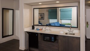 Un baño moderno con un espejo grande, un lavabo, una cafetera y un microondas.