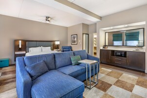 Una habitación de hotel con sofá modular, cama, escritorio, kitchenette y baño.