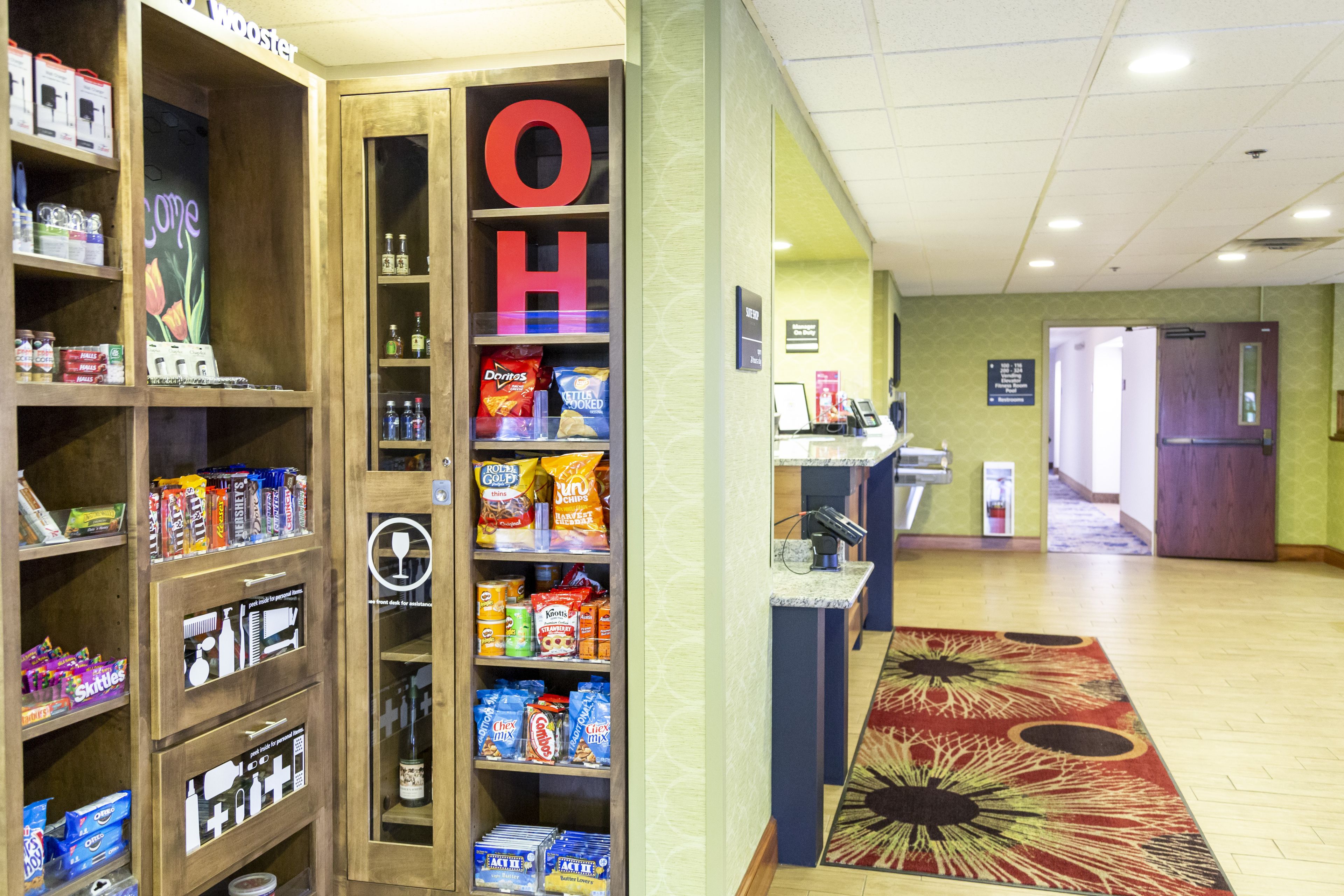 A hotel lobby with a reception desk, a large 'OH' sign, and shelves stocked with snacks and beverages.