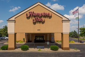 Edificio de Hampton Inn con fachada color beige, entrada destacada y bandera estadounidense.