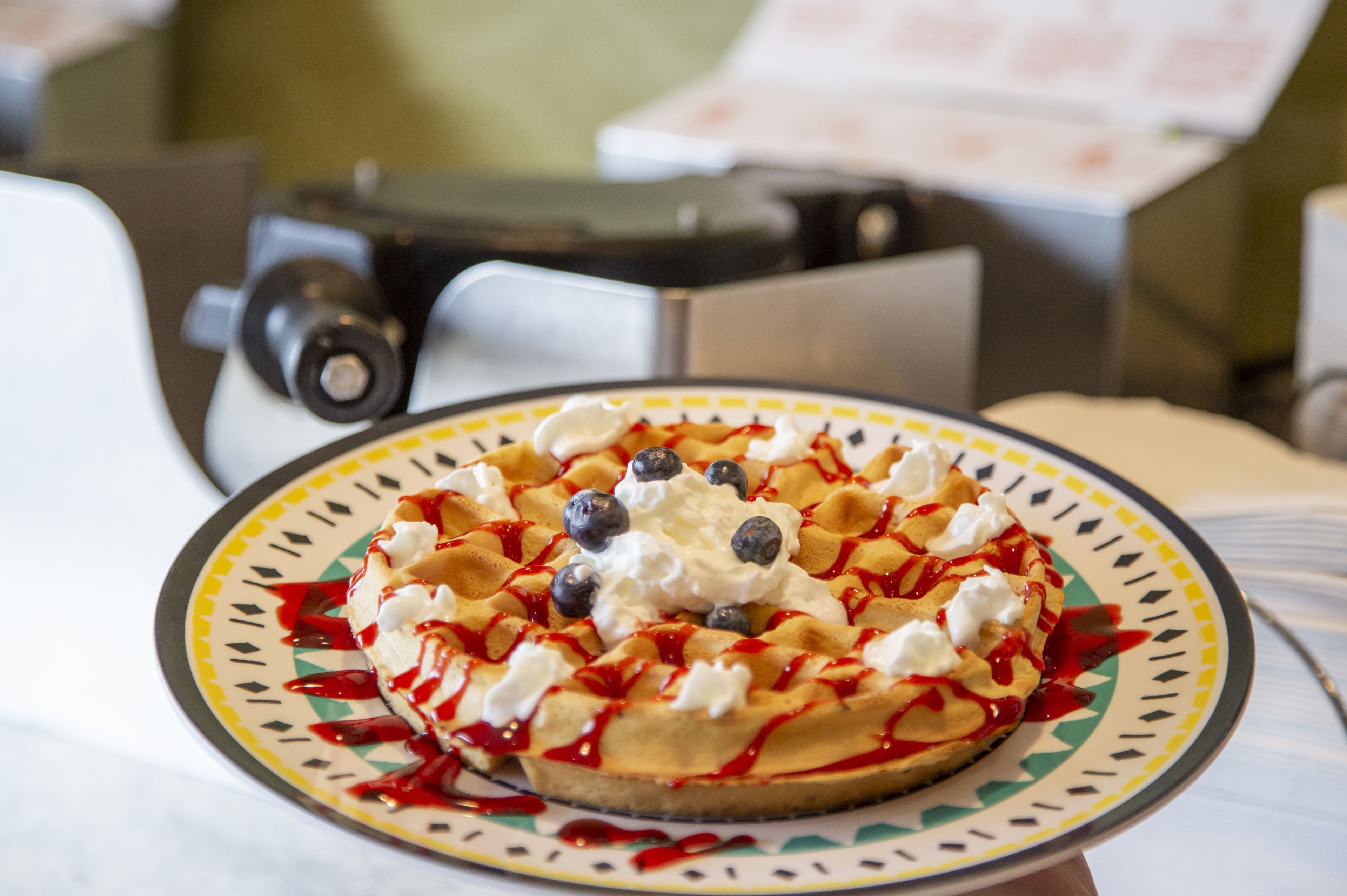 A waffle with whipped cream and blueberries on a plate.