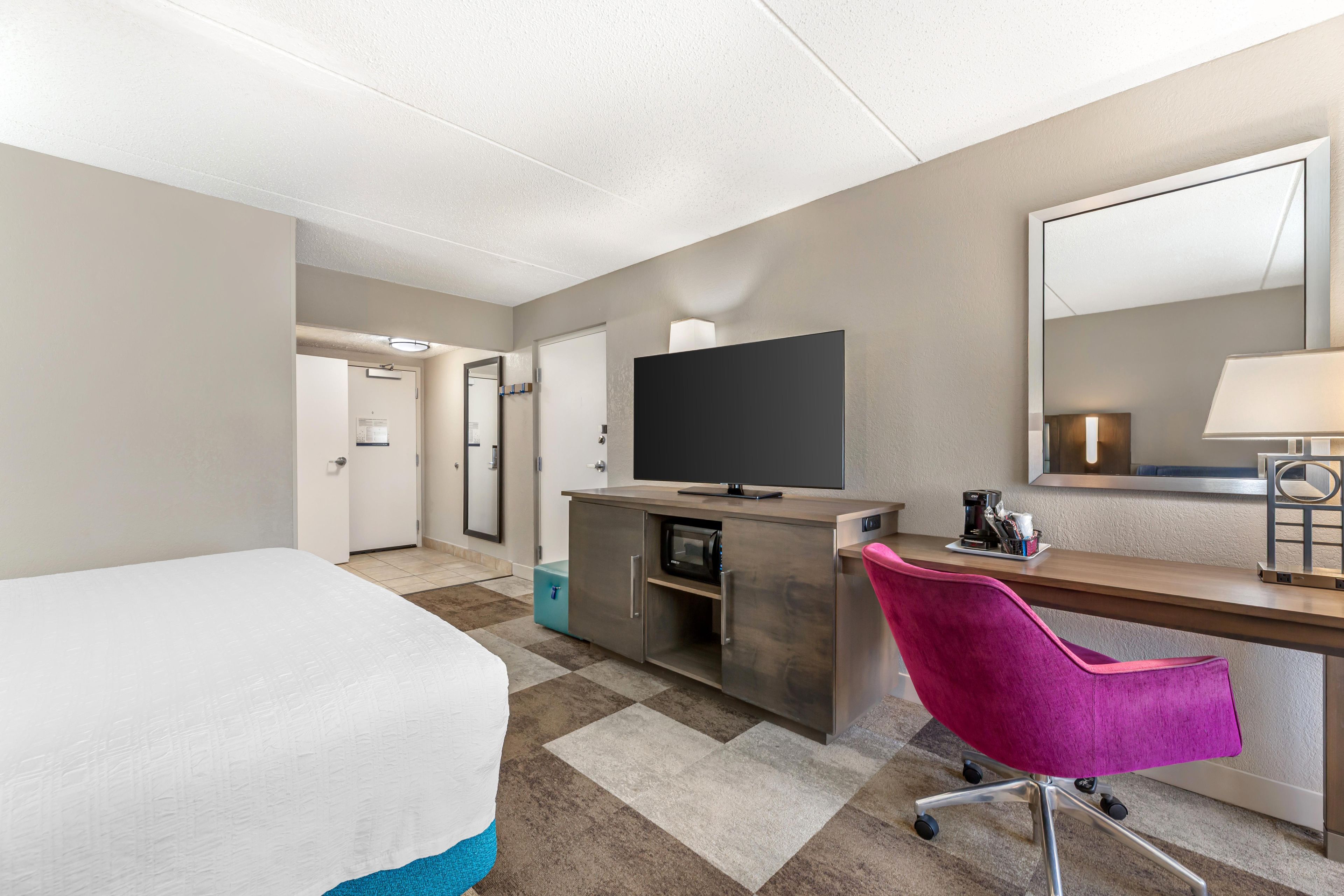 Een hotelkamer met een bed, een bureau met een computer, een stoel, een televisie en een koffiezetapparaat.