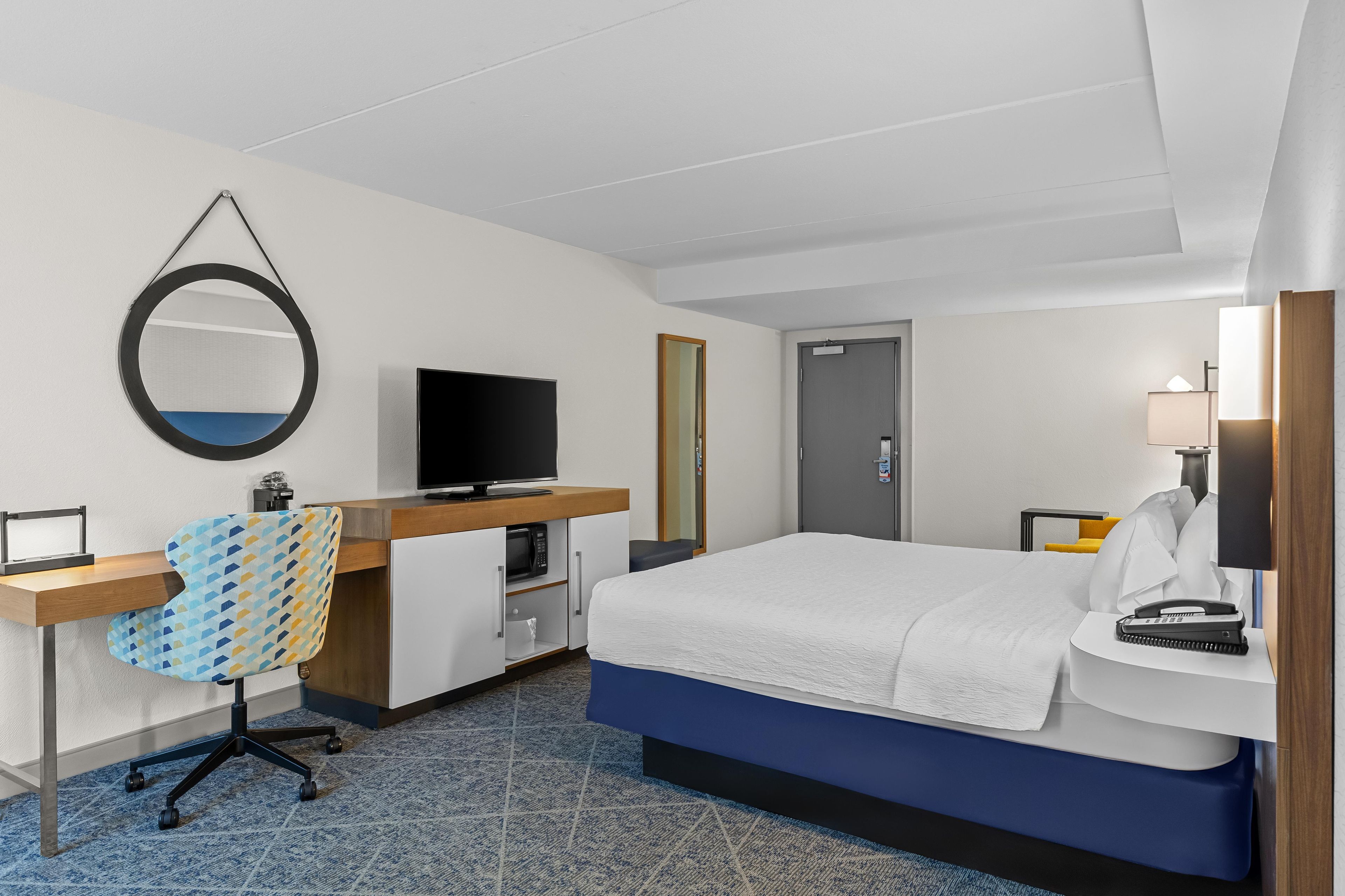 Ein Hotelzimmer mit Bett, Schreibtisch, Fernseher und Spiegel.