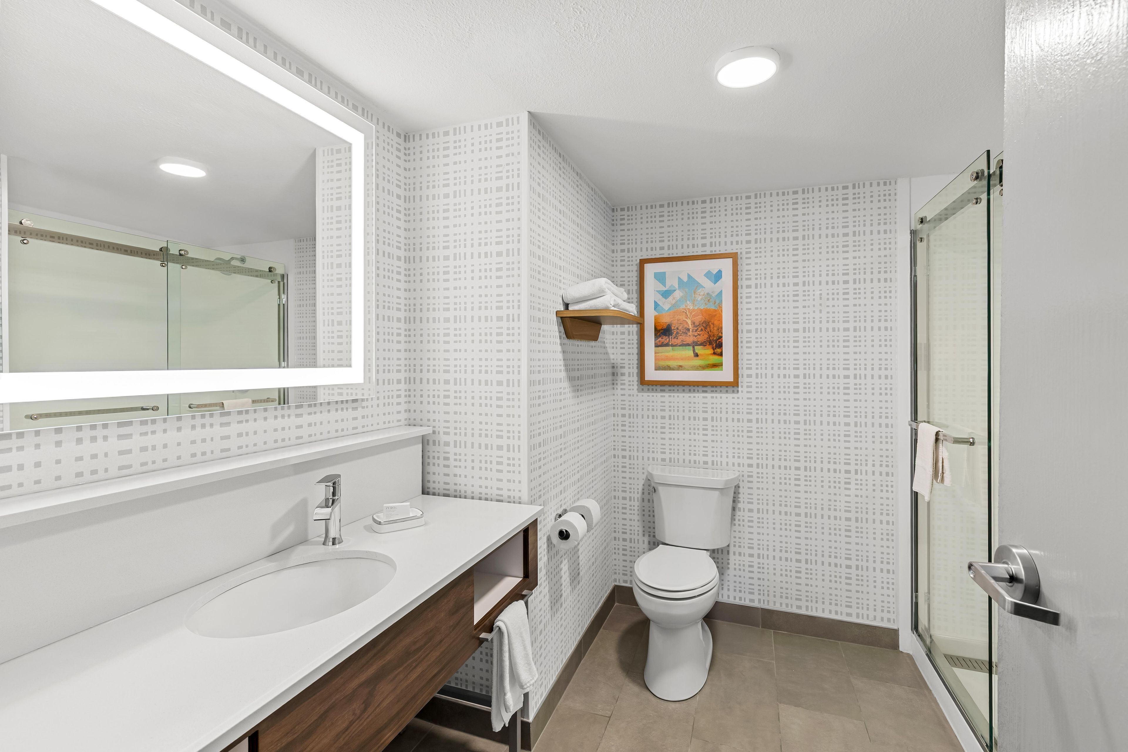 A bathroom with a large mirror, a sink, a toilet, and a shower area.