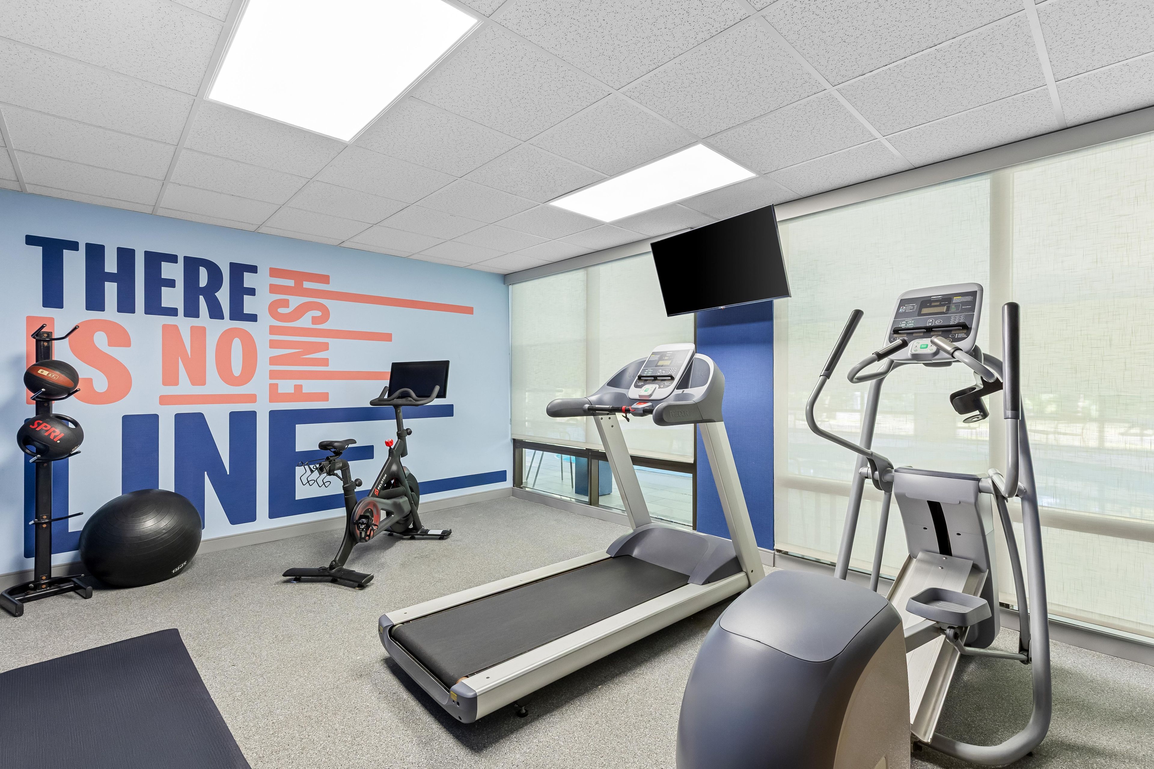 Et fitnesscenter med træningsudstyr, en motiverende væg og store vinduer.
