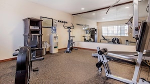 A gym with exercise equipment, a mirror, and a wall-mounted shelf with folded towels. - Quality Inn & Suites Owasso US-169 (Owasso)