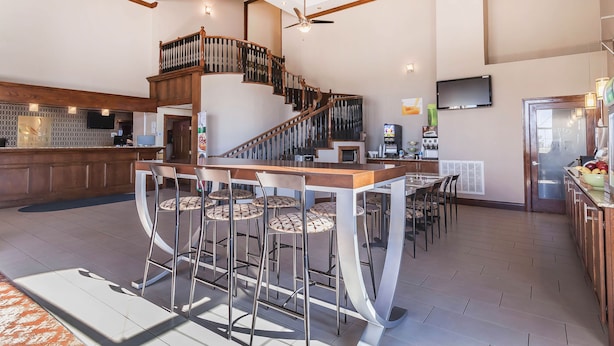 A spacious kitchen with a central island, a bar area with stools, a staircase, and a TV mounted on the wall. - Quality Inn & Suites Owasso US-169 (Owasso)