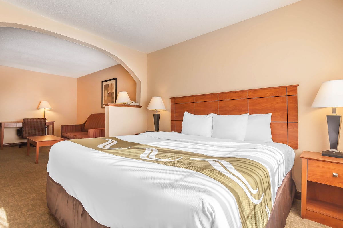 A hotel room with a large bed, a wooden headboard, two bedside tables with lamps, a desk, and a chair.