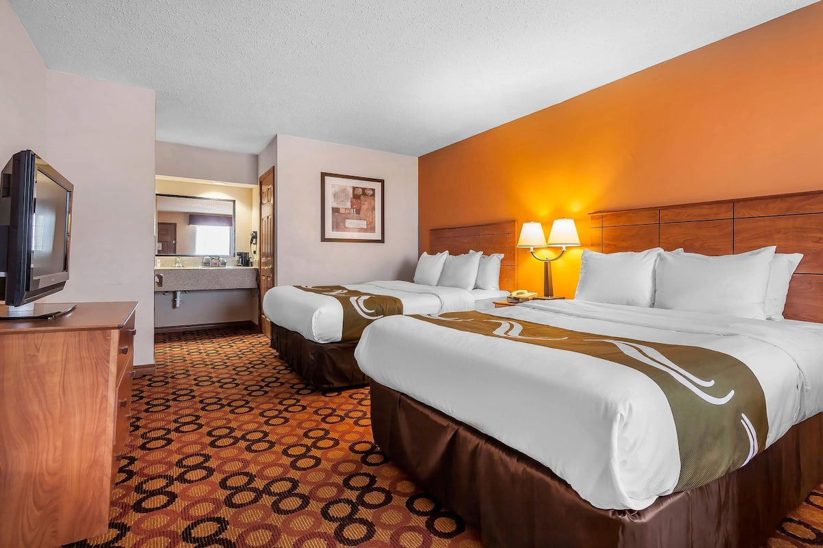 A hotel room with two beds, a TV, a bathroom, and a patterned carpet.