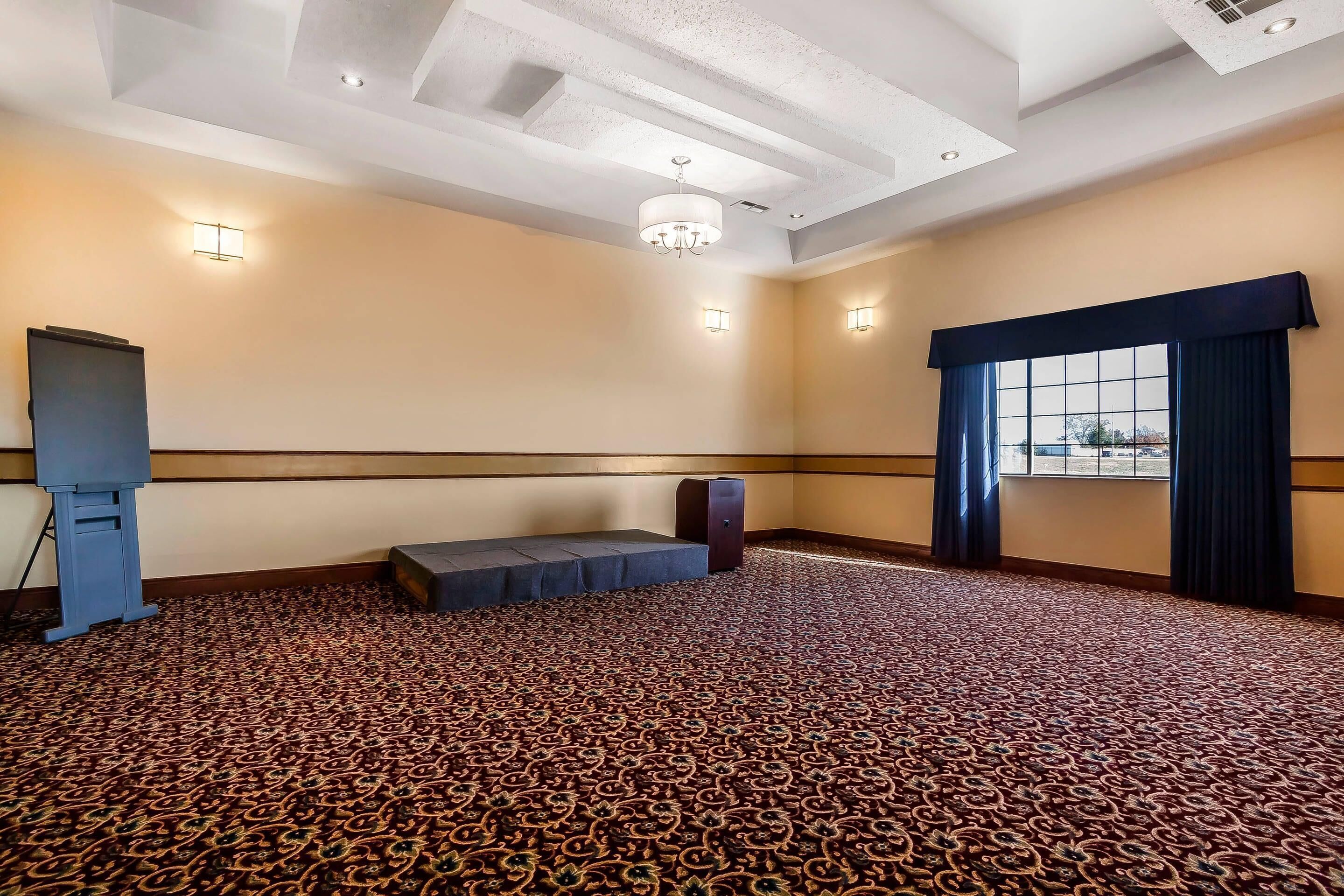 A spacious room with a patterned carpet, a bench, a podium, and a large window with curtains.
