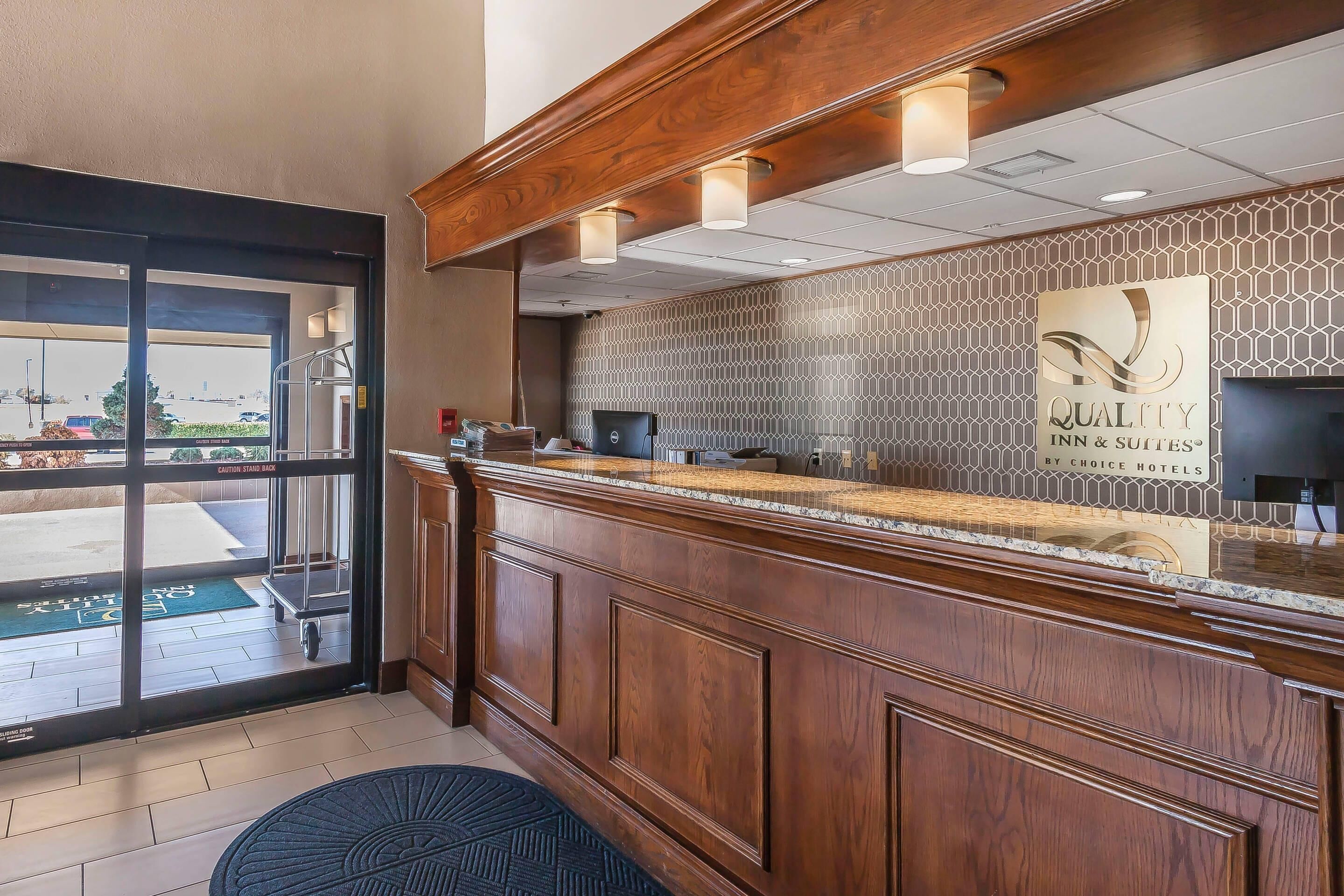 A reception area with a wooden counter, a patterned wall, and a sign that reads "QUALITY INN & SUITES BY CHOICE HOTELS".