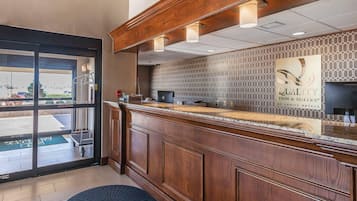 A reception area with a wooden counter, a patterned wall, and a sign that reads "QUALITY INN & SUITES BY CHOICE HOTELS".