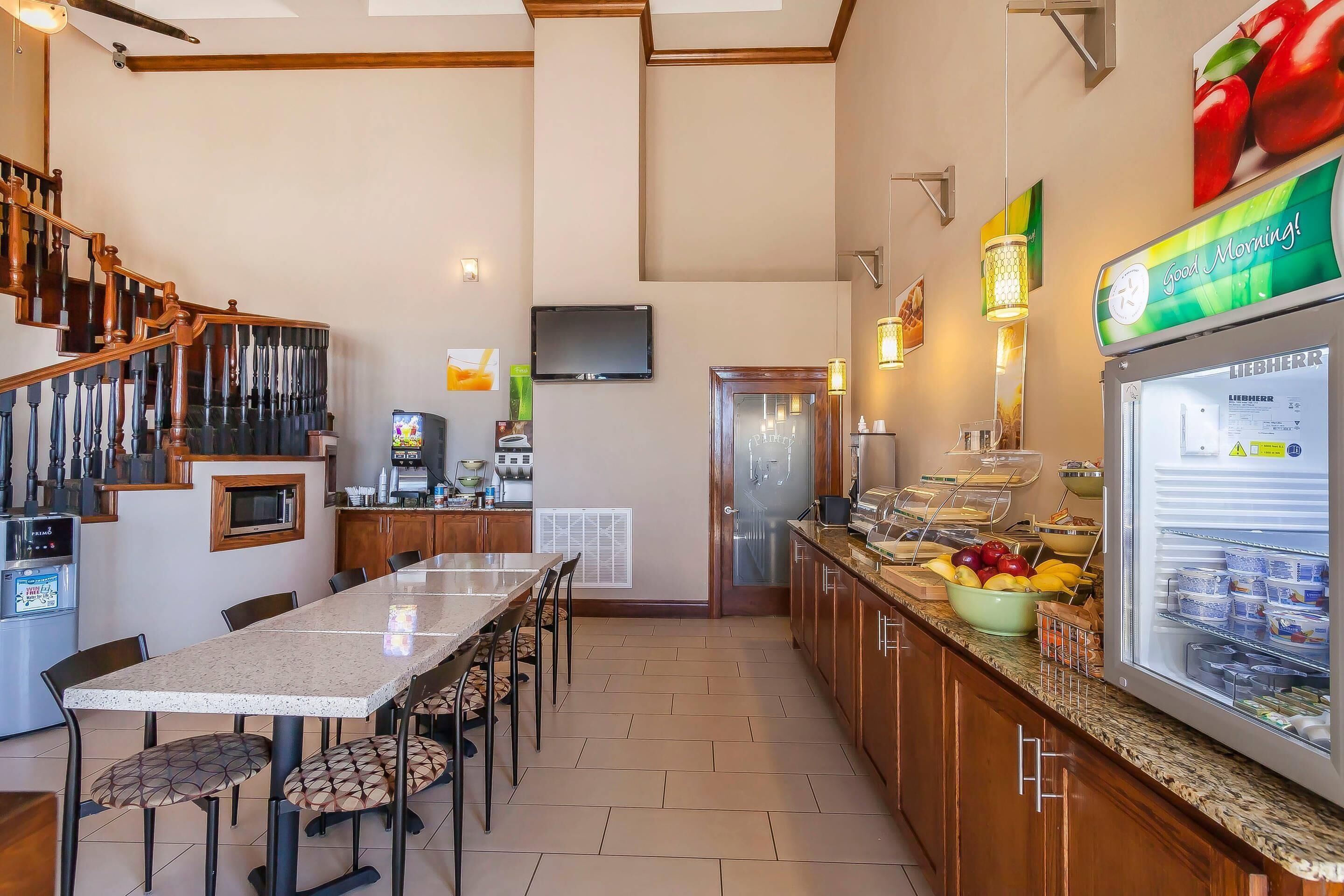 A hotel kitchen with a dining area, a refrigerator with food, a television, and a staircase.