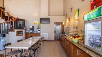 A hotel kitchen with a dining area, a refrigerator with food, a television, and a staircase.