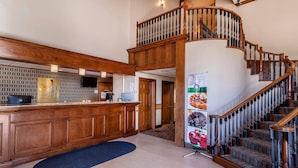 A hotel lobby with a wooden reception desk, a staircase, and a wall-mounted television. - Quality Inn & Suites Owasso US-169 (Owasso)