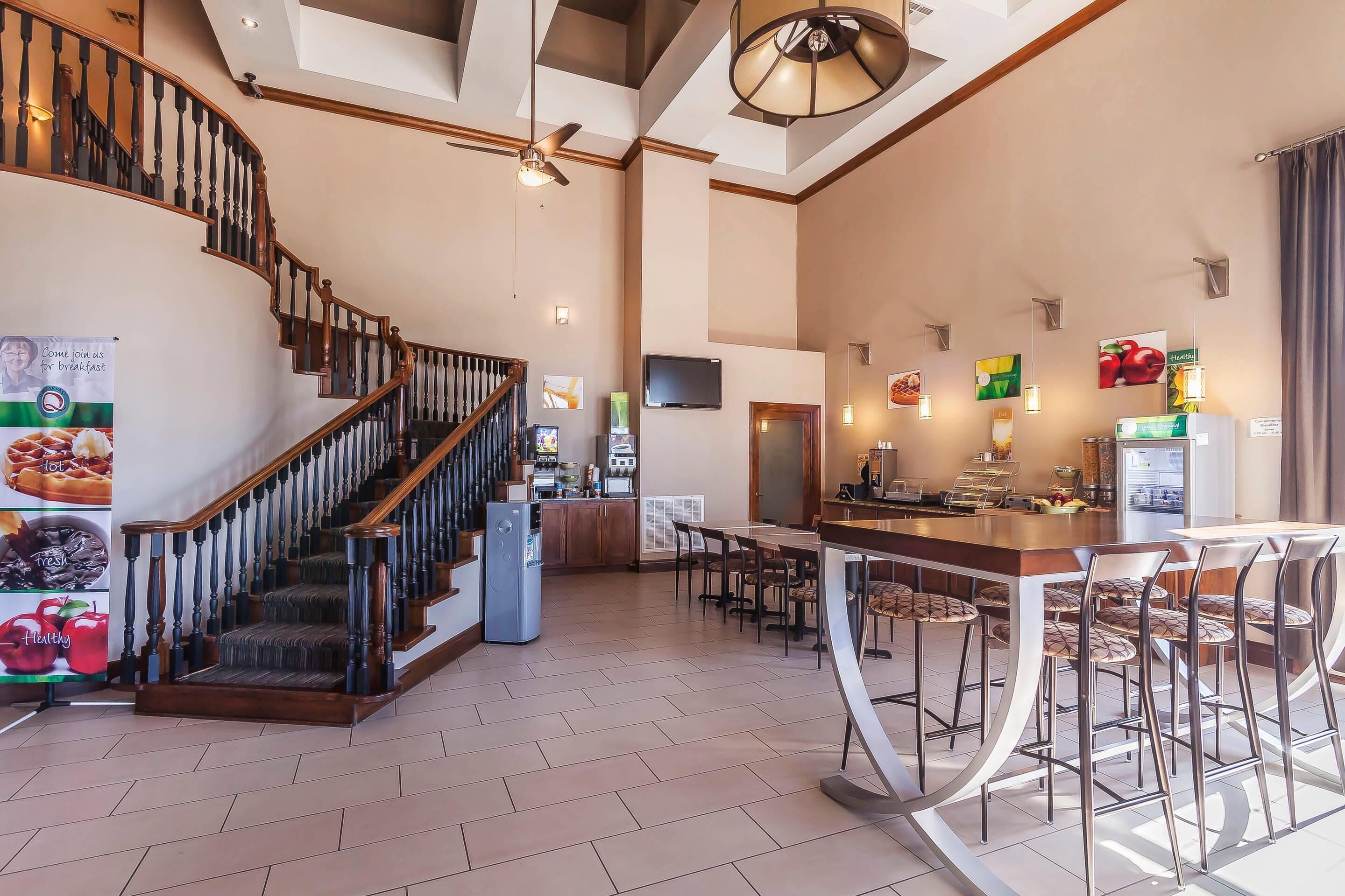 A spacious kitchen with a central island, a dining area with bar stools, a staircase with wooden railings, and a ceiling fan.