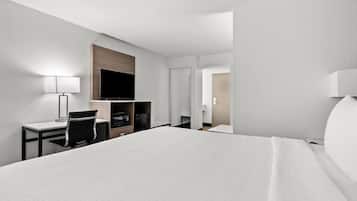 Une chambre d’hôtel dotée d’un grand lit, d’un bureau avec une chaise, d’un téléviseur à écran plat fixé au mur, d’un four à micro-ondes et d’un réfrigérateur.