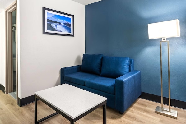 A room with a blue sofa, a small table, a floor lamp, and a framed picture on the wall. - Baymont by Wyndham Ardmore I-35 (Ardmore)