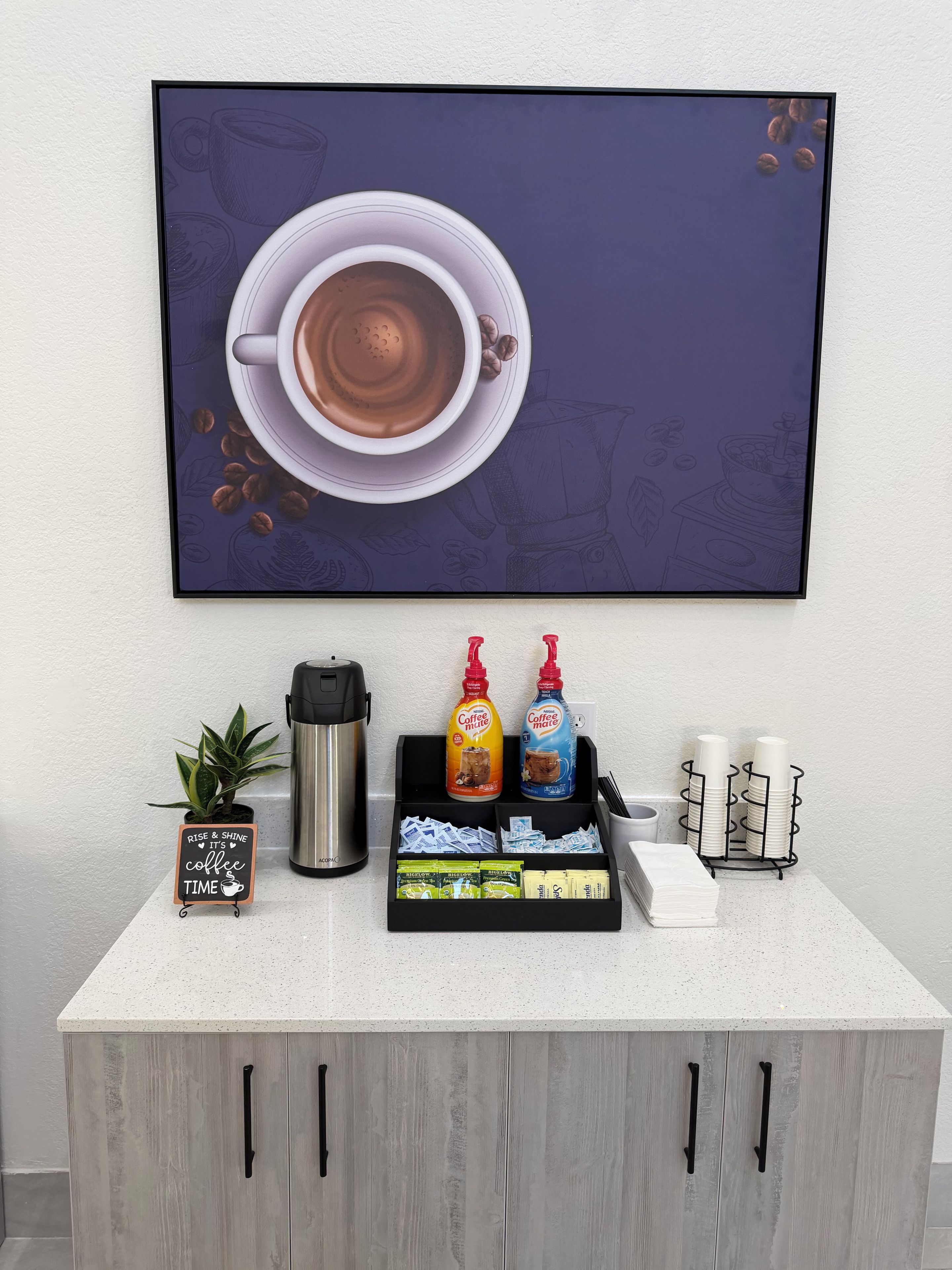 Ein Kaffee-Bereich mit einer Kaffeemaschine, zwei Kaffeezubereitern, einem Schild und einer Pflanze.