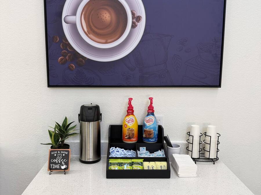 A coffee station with a coffee machine, two coffee makers, a sign, and a plant.