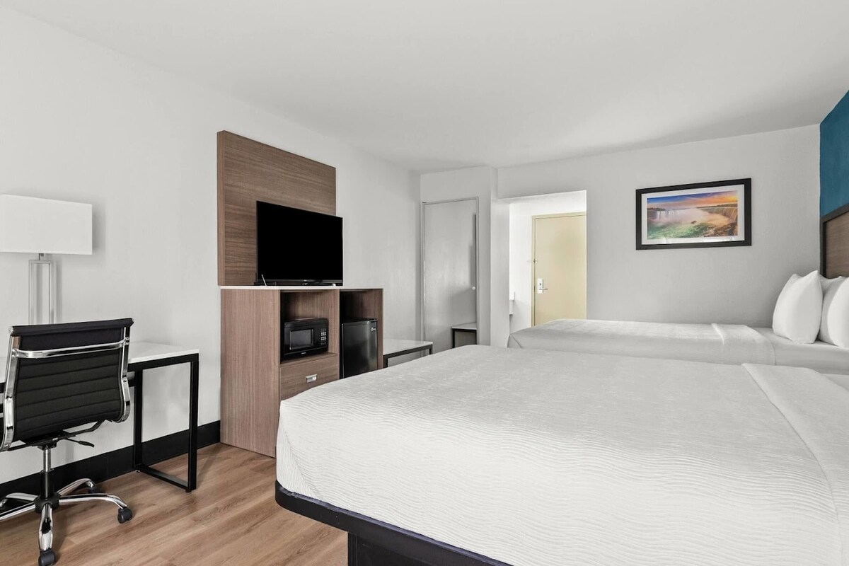 Una habitación de hotel con cama, escritorio con silla, televisor, microondas y refrigerador.