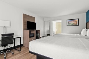 Una habitación de hotel con cama, escritorio con silla, televisor, microondas y refrigerador.