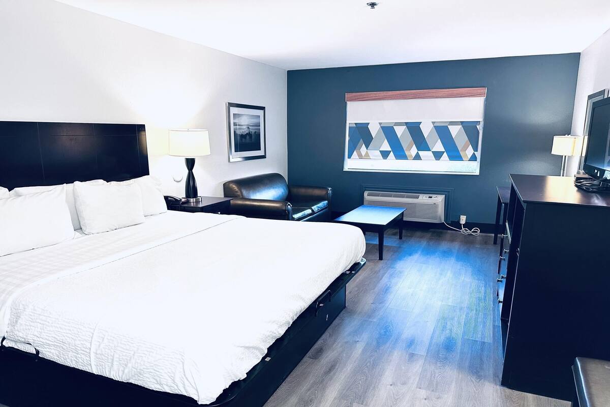 Habitación de hotel con una cama grande, un escritorio, una silla, un televisor y un ventanal con un diseño geométrico.