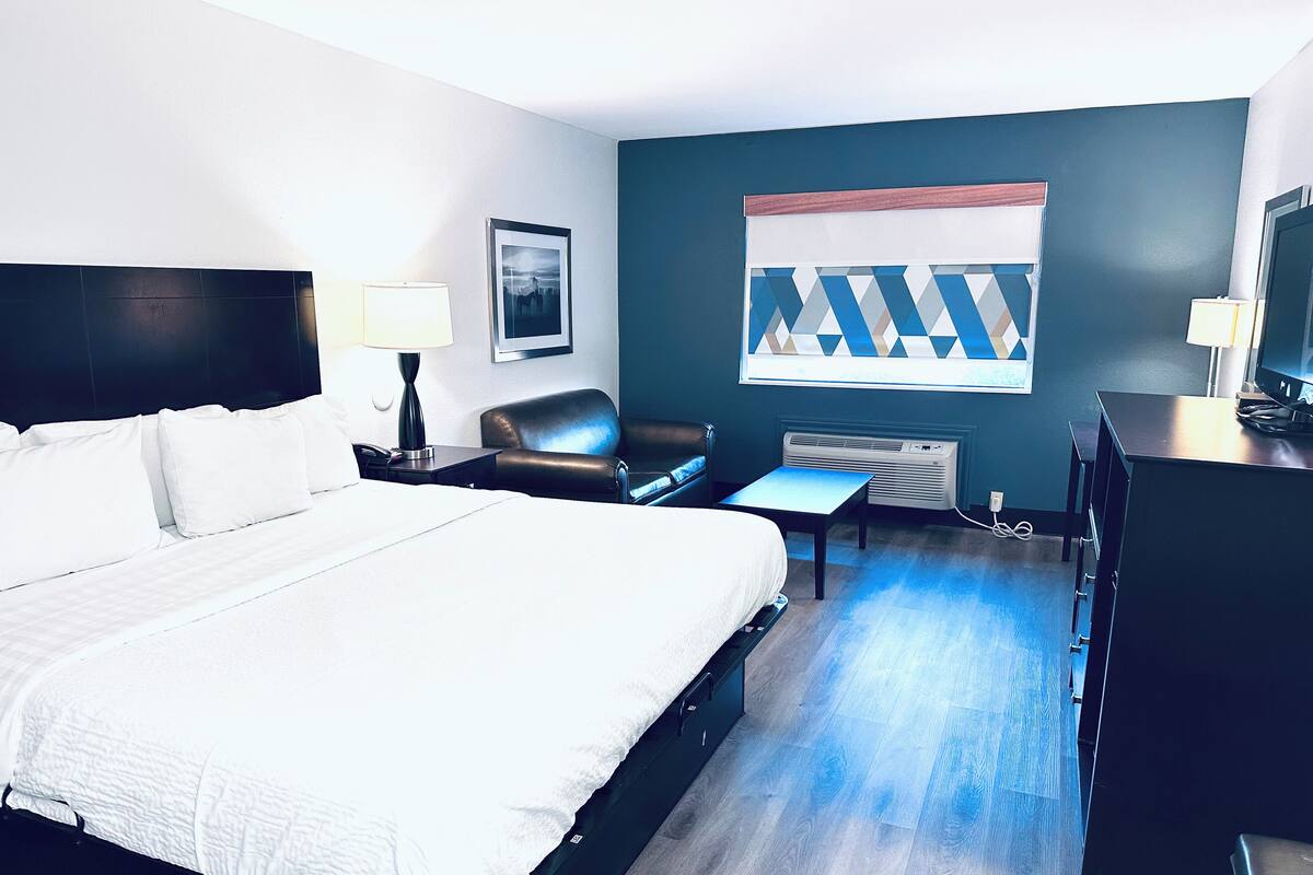 Habitación de hotel con una cama grande, un escritorio, una silla, un televisor y una ventana con vistas geométricas.