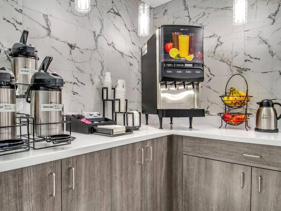 Une cuisine moderne équipée d’une machine à café intégrée, d’un distributeur de jus de fruits et d’une bouilloire.