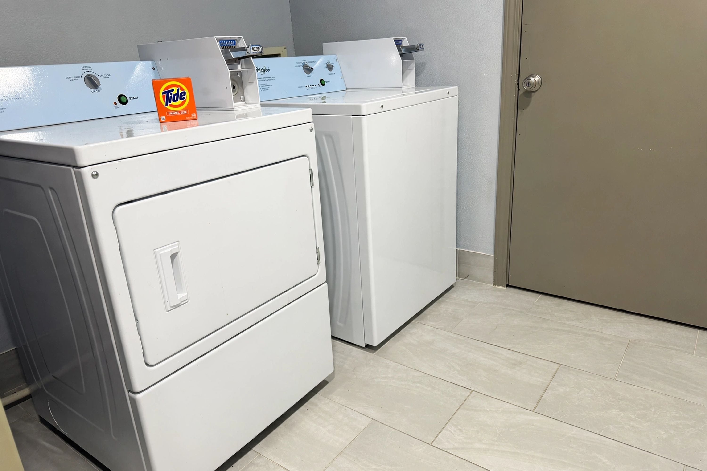 Une buanderie équipée de deux machines à laver et deux sèche-linge superposés, d’une boîte de lessive Tide et d’une porte.